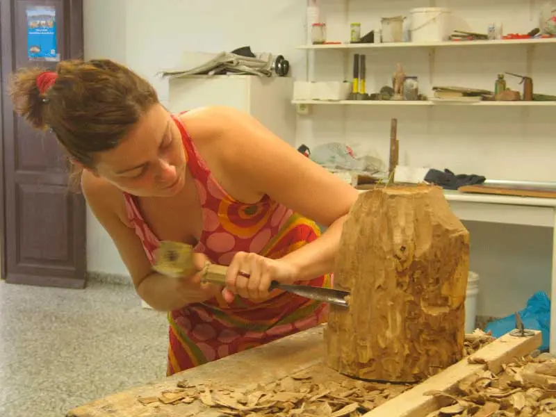 Alumna tallando un tronco de madera con mazo y gubia