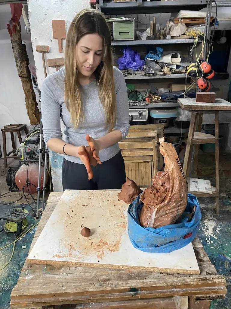 Alumna modelando una figura en barro sobre una mesa de trabajo del taller