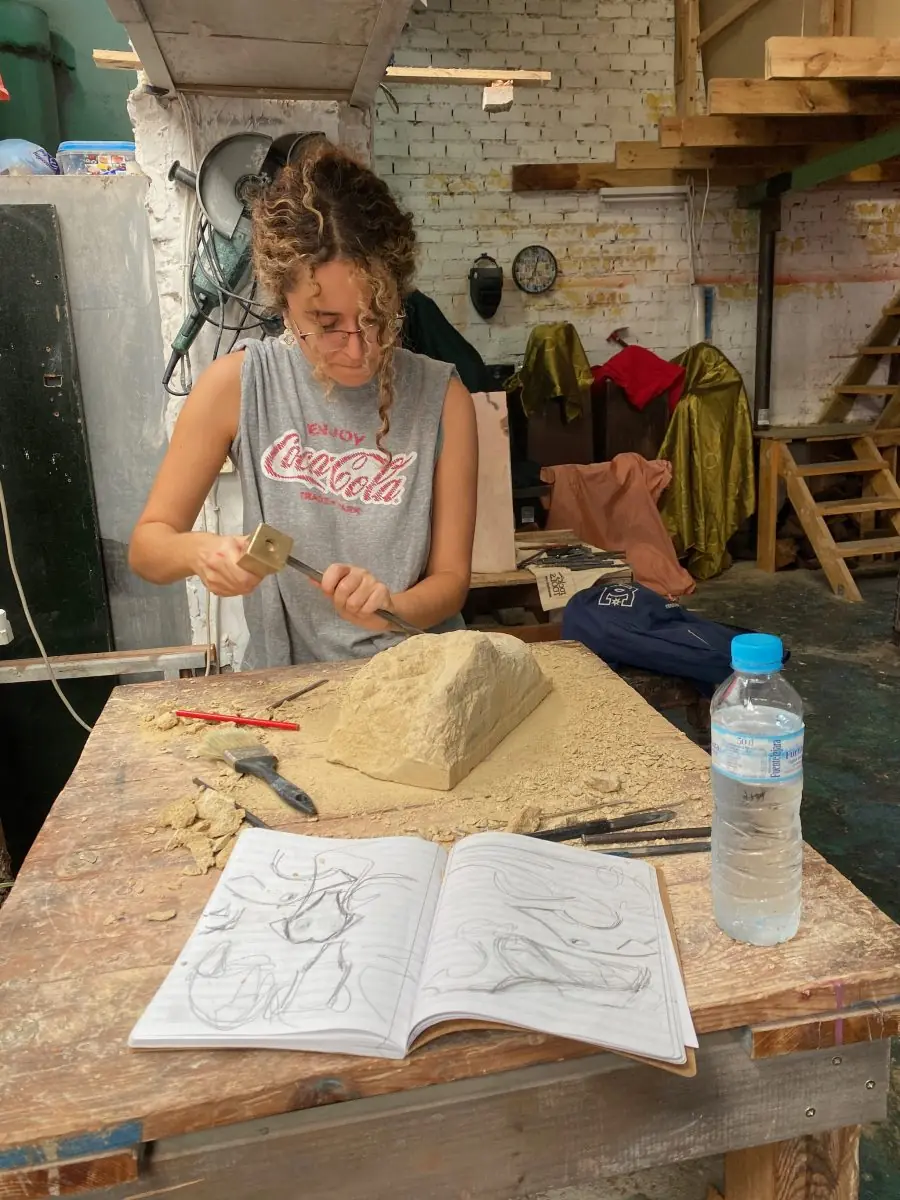 Alumna tallando un bloque de piedra con martillo y puntero en el taller