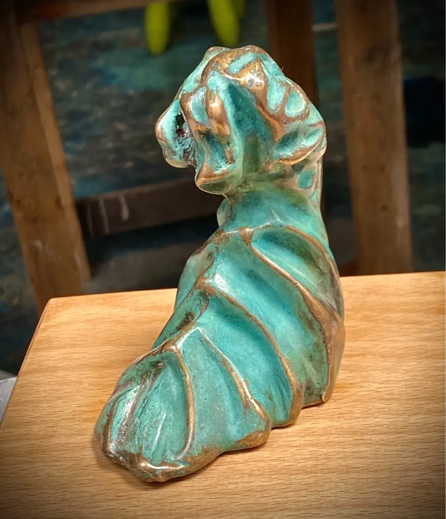 Escultura en bronce con pátina verde y forma de ola sobre una base de madera